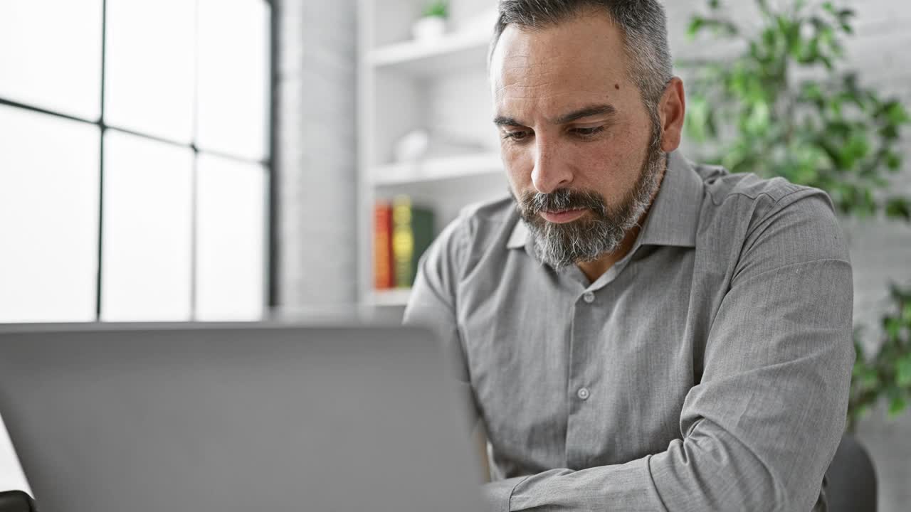 成熟的大胡子男人在现代办公场所用笔记本电脑工作。视频下载