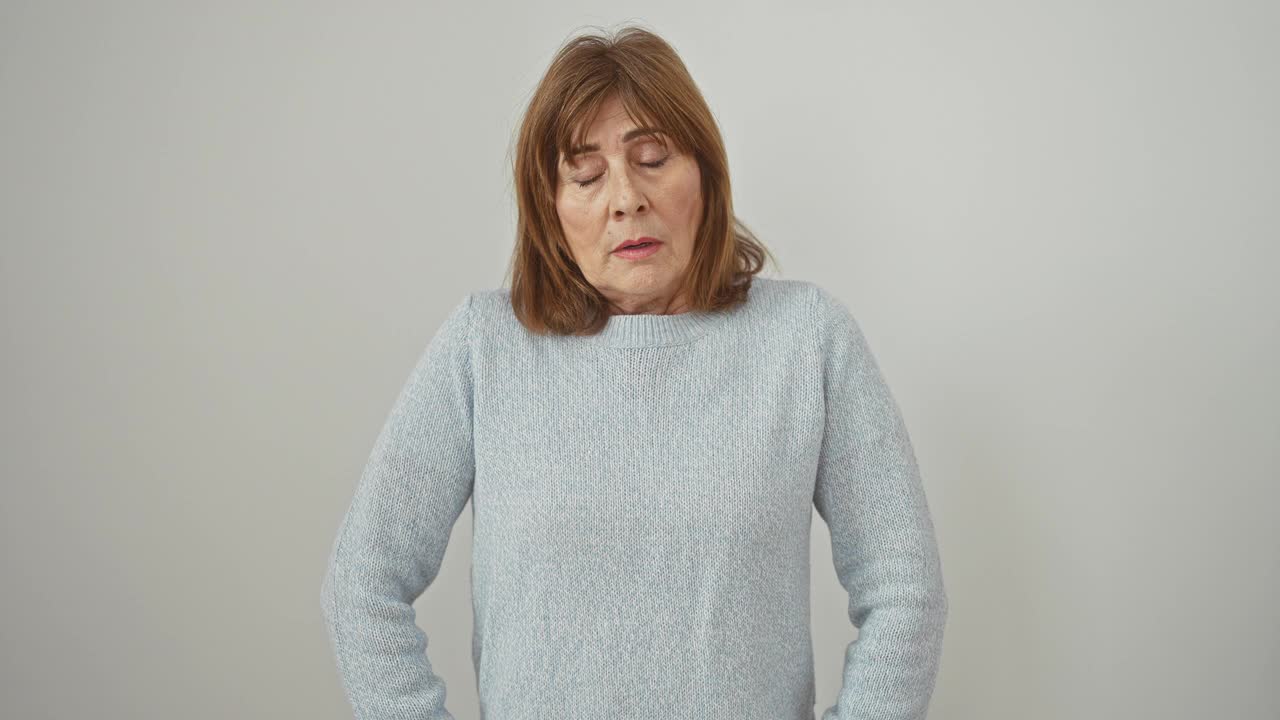 一个穿着毛衣、疲惫不堪的中年妇女，睡眼惺忪，反映出宿醉后的疲惫，独自站在白色的背景上，这是第二天早上。视频下载