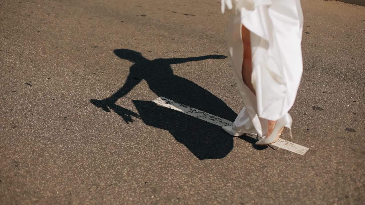 一个女孩穿着裙子，张开双臂走在路中央。她的影子美丽地落在柏油路上视频下载