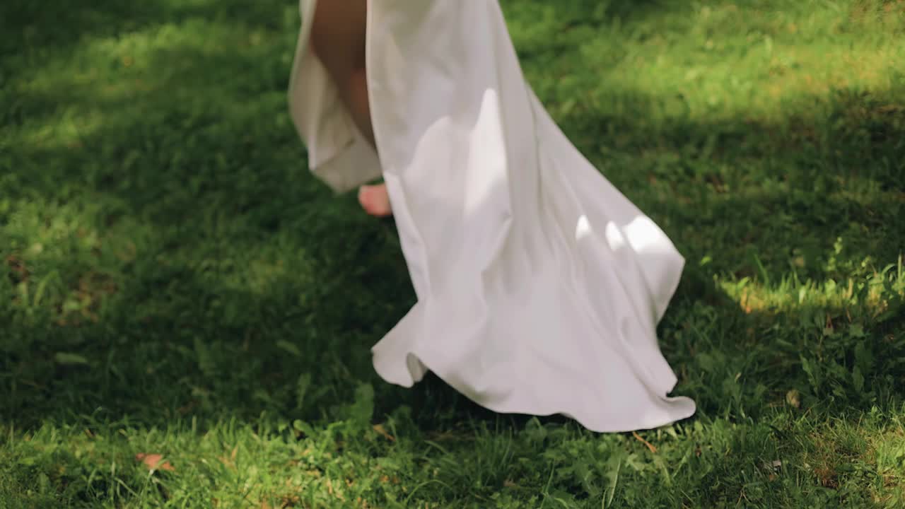 一个穿着白色长裙的女孩跑过草地。用慢镜头拍她的腿视频下载