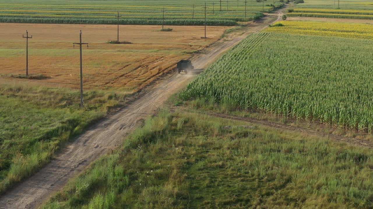 无人机拍摄的夏日午后，拖拉机和拖车沿着乡间的土路行驶，穿过耕地视频素材