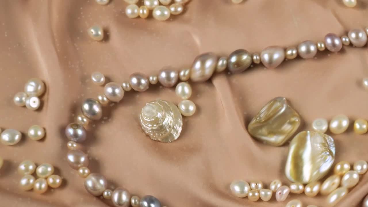 天然珍珠和由珍珠和珍珠母制成的珠宝，在米色的水下背景。在清澈的水面上泛起涟漪。视频下载