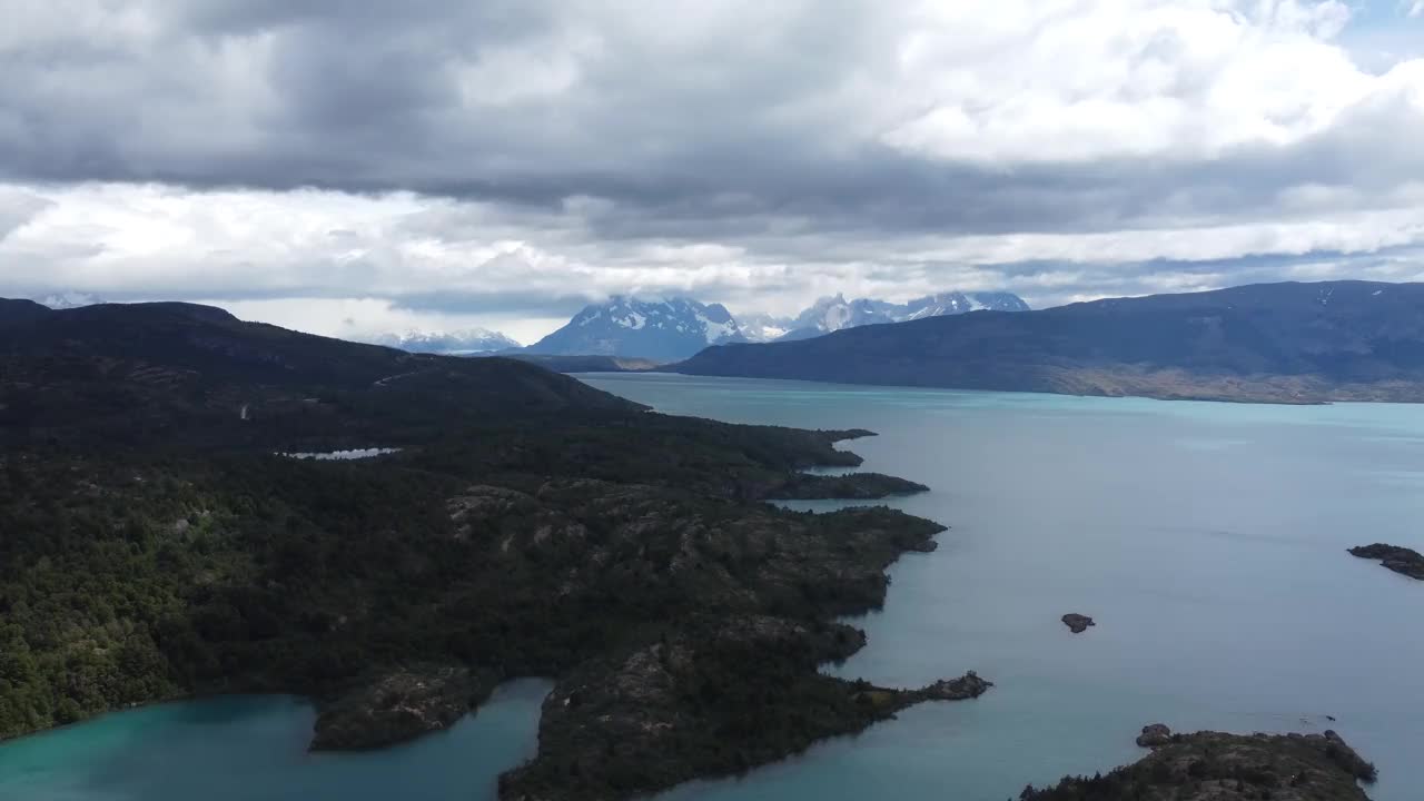 镜头从多云的天空向下平移到智利托雷斯德尔潘恩国家公园的蓝色湖泊，远处是湖泊和白雪皑皑的山脉视频下载
