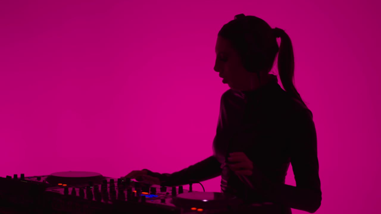 女DJ在耳机混合轨道的现代电子音乐，肖像在粉红色的背景视频下载