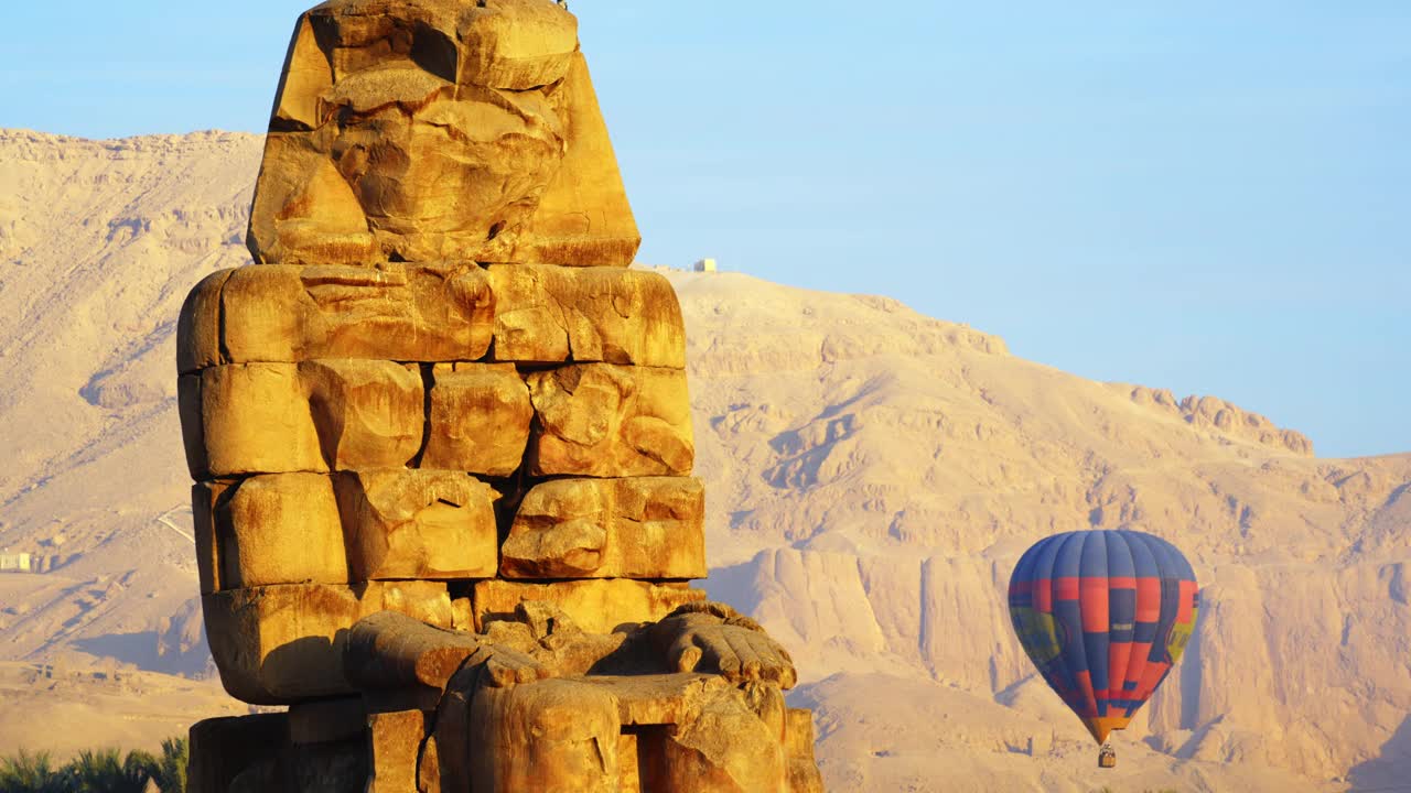 黎明时分，埃及尼罗河谷卢克索，天空中有热气球的门农巨像。视频下载