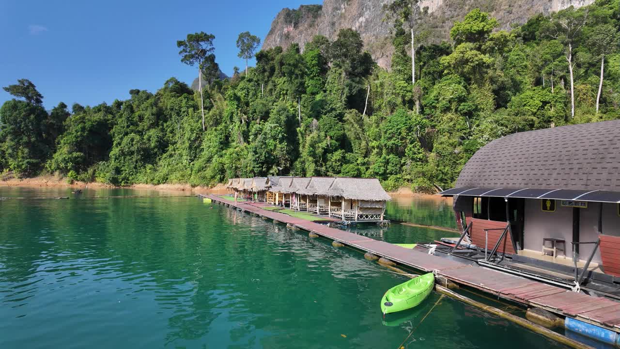 泰国素叻他尼的考索国家公园(Khao Sok National Park)充满活力的海岸线风景，在郁郁葱葱的绿色植物和雄伟的山脉的背景下，一座沿海漂浮的小屋。视频下载