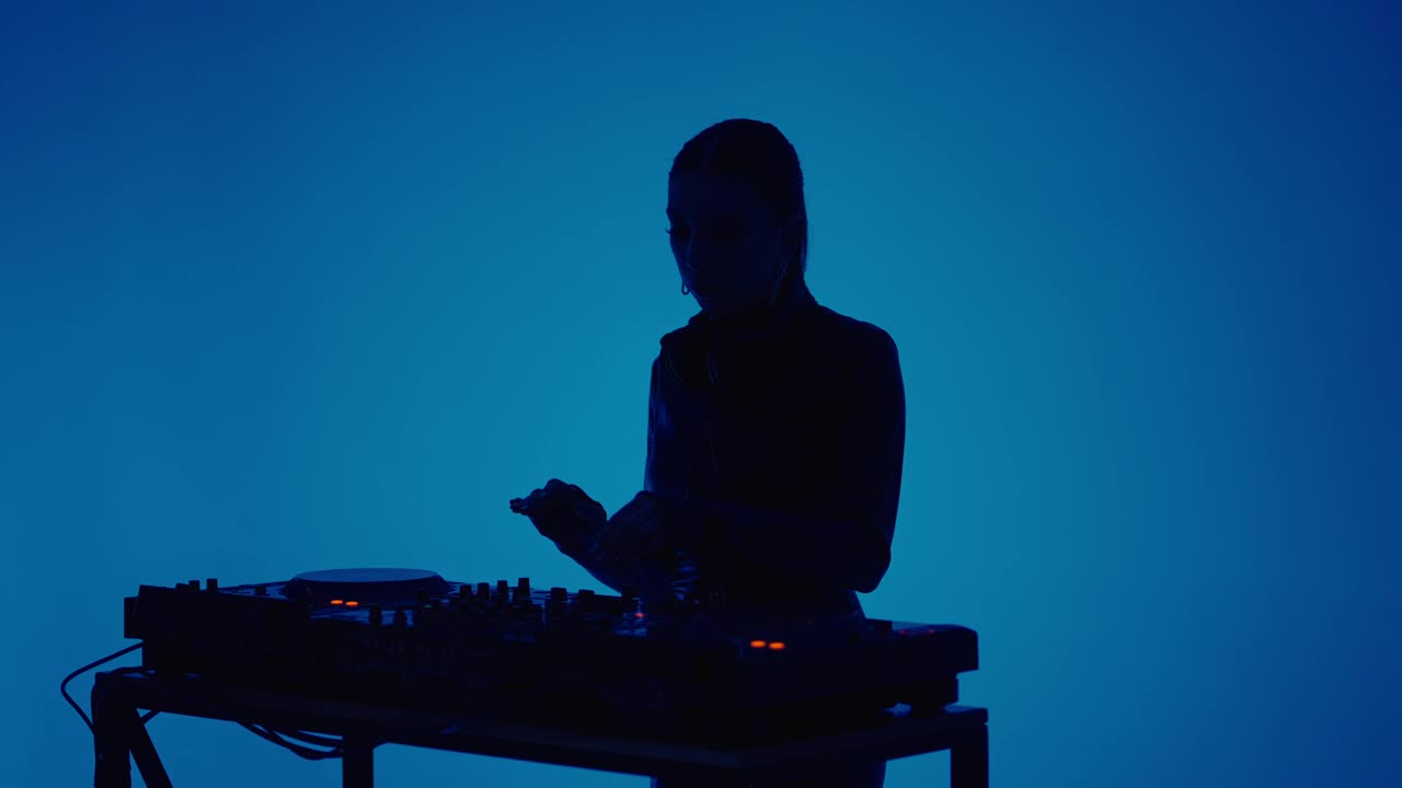 性感女士DJ跳舞和混合轨道的现代电子音乐，剪影肖像在蓝色视频下载
