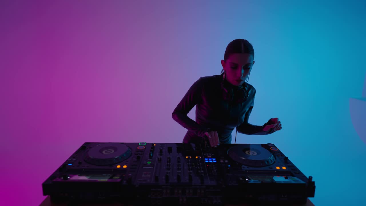 美丽的黑发女子DJ混合轨道在工作室与蓝色和粉红色的背景，中等肖像视频下载