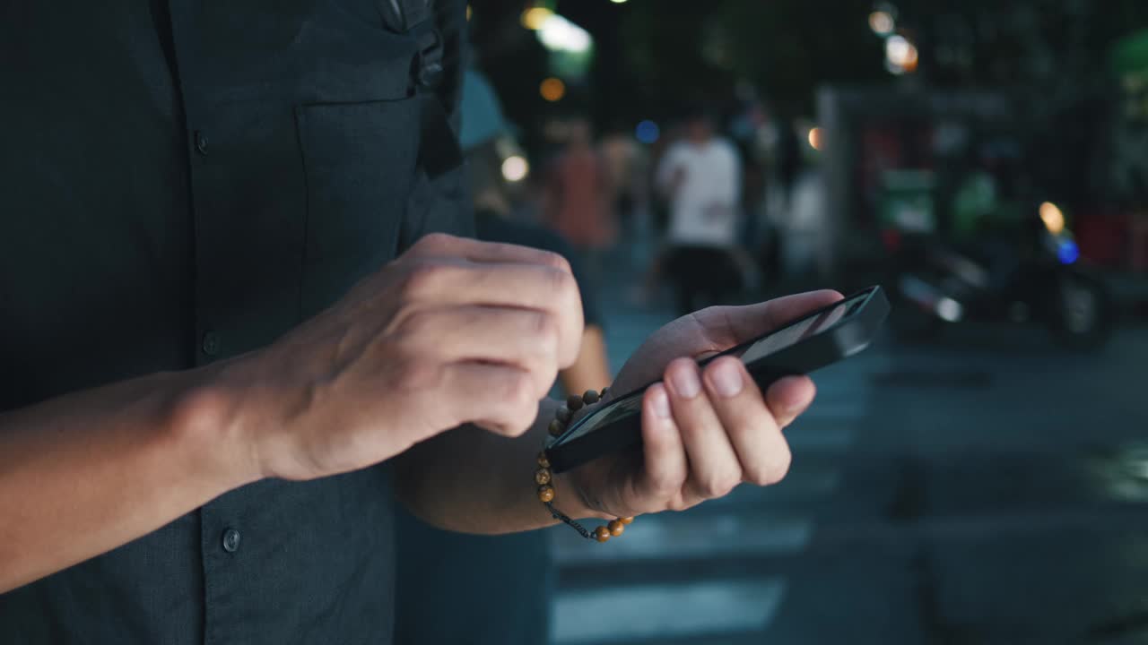 特写男子操作智能手机的手，象征着现代城市连接的时代，重点是社交媒体互动，移动互联网和消息传递。城市景观和智能手机使用概念视频下载