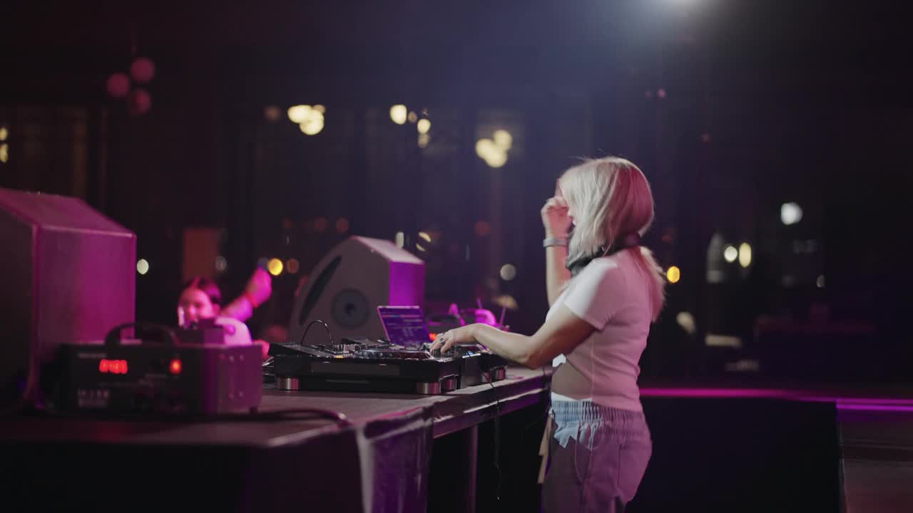 欢乐的舞会在夜总会，漂亮的金发女郎DJ摇摆人群在舞池，混音轨道视频下载