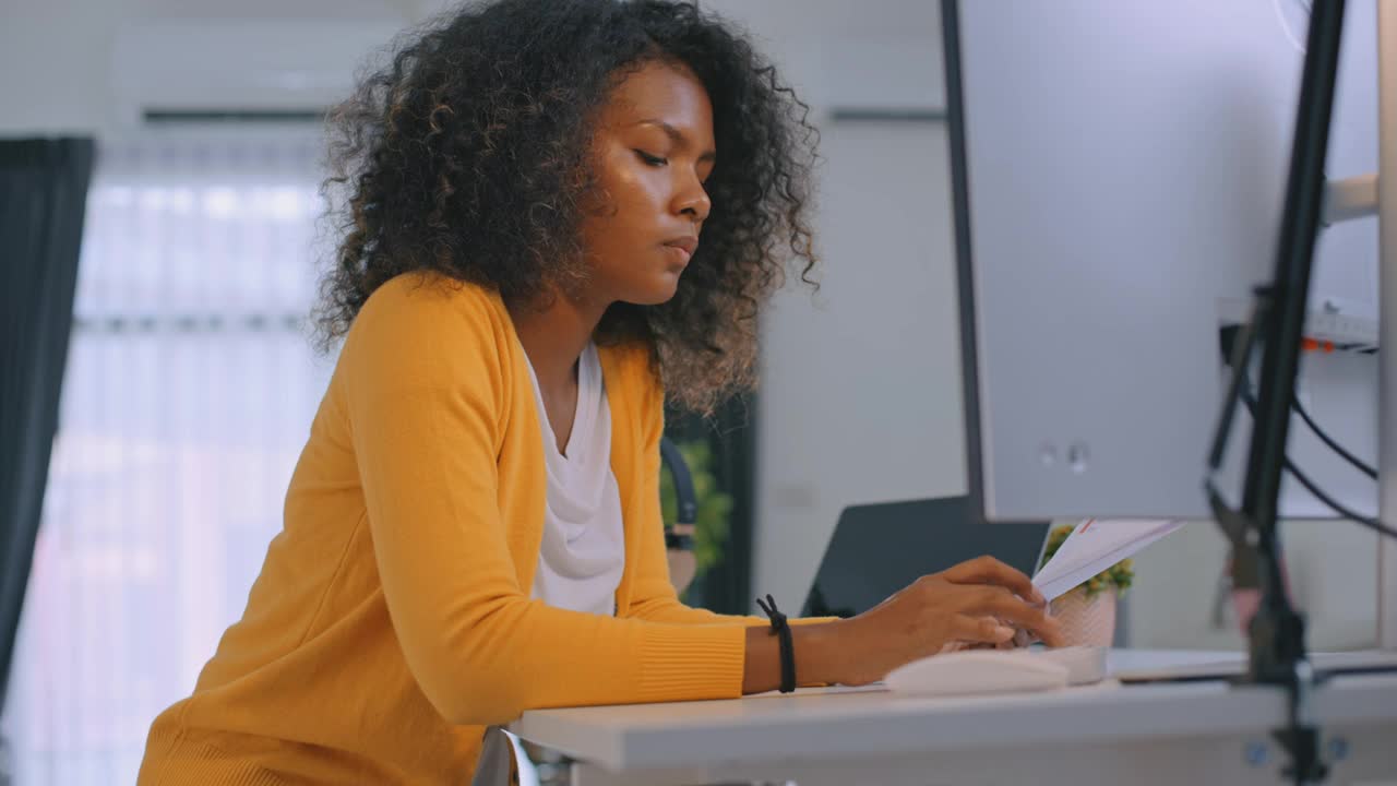 一头非洲发型的自信女商人在办公桌前使用电脑。女企业家在家工作。她在远程办公。视频下载