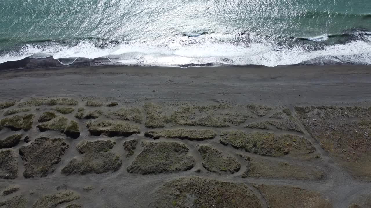 镜头向下看，海浪拍打着黑色的沙滩，深绿色的大海视频下载