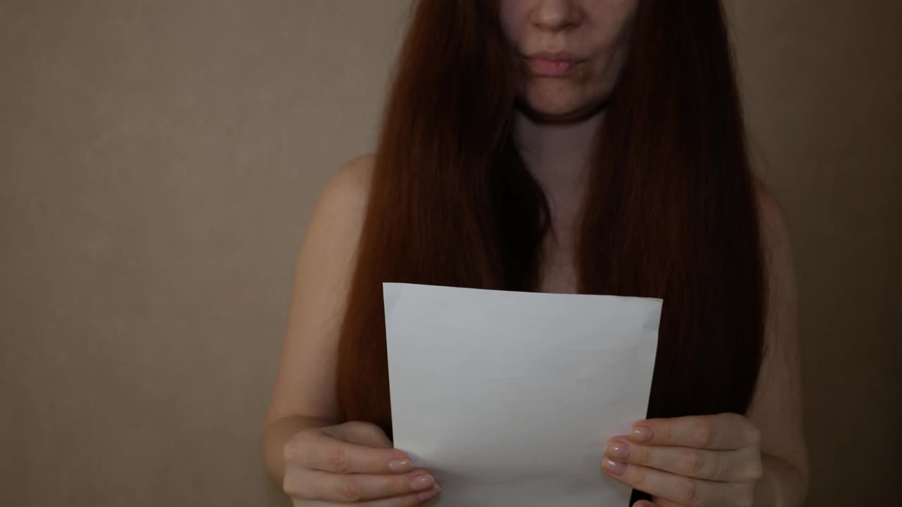 一个年轻女子拿着一张白纸，读着一封信，然后把它撕成碎片。视频下载