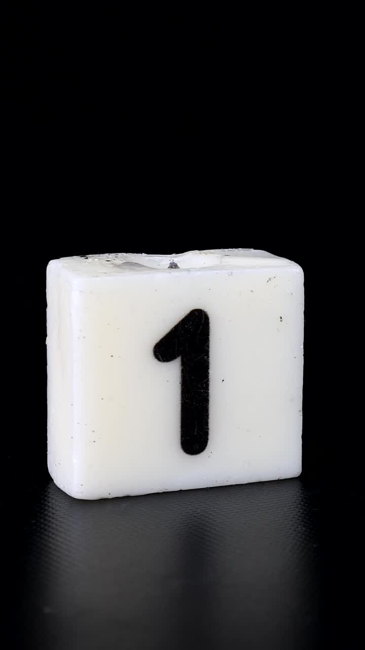 一个写着数字1的正方形蜡烛被点燃，然后在黑色背景上被吹灭，庆祝生日或周年纪念日视频下载