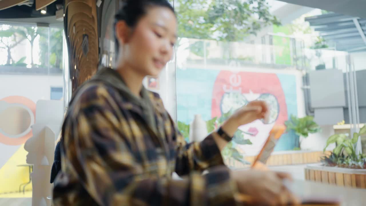 亚洲女性在咖啡店愉快地使用平板电脑和智能手机，使用现代互联网通信技术视频下载