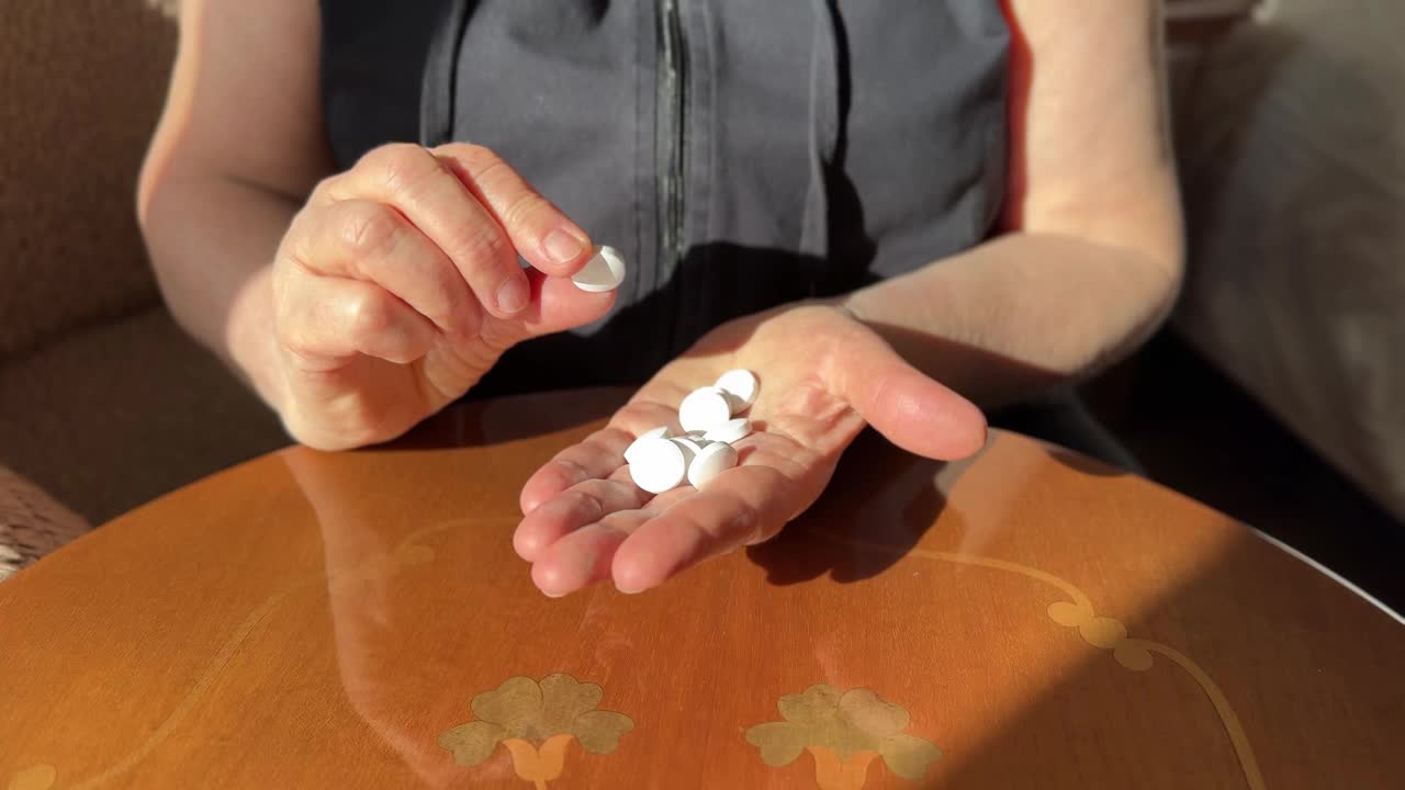 一位老年妇女的手的特写，她在手里选择不同的药片视频下载