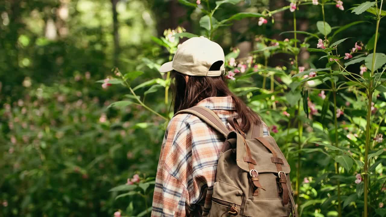 年轻的白人妇女背着背包在森林里旅行。这个女孩在大自然中感到清新、美妙、兴奋和放松。慢动作视频下载