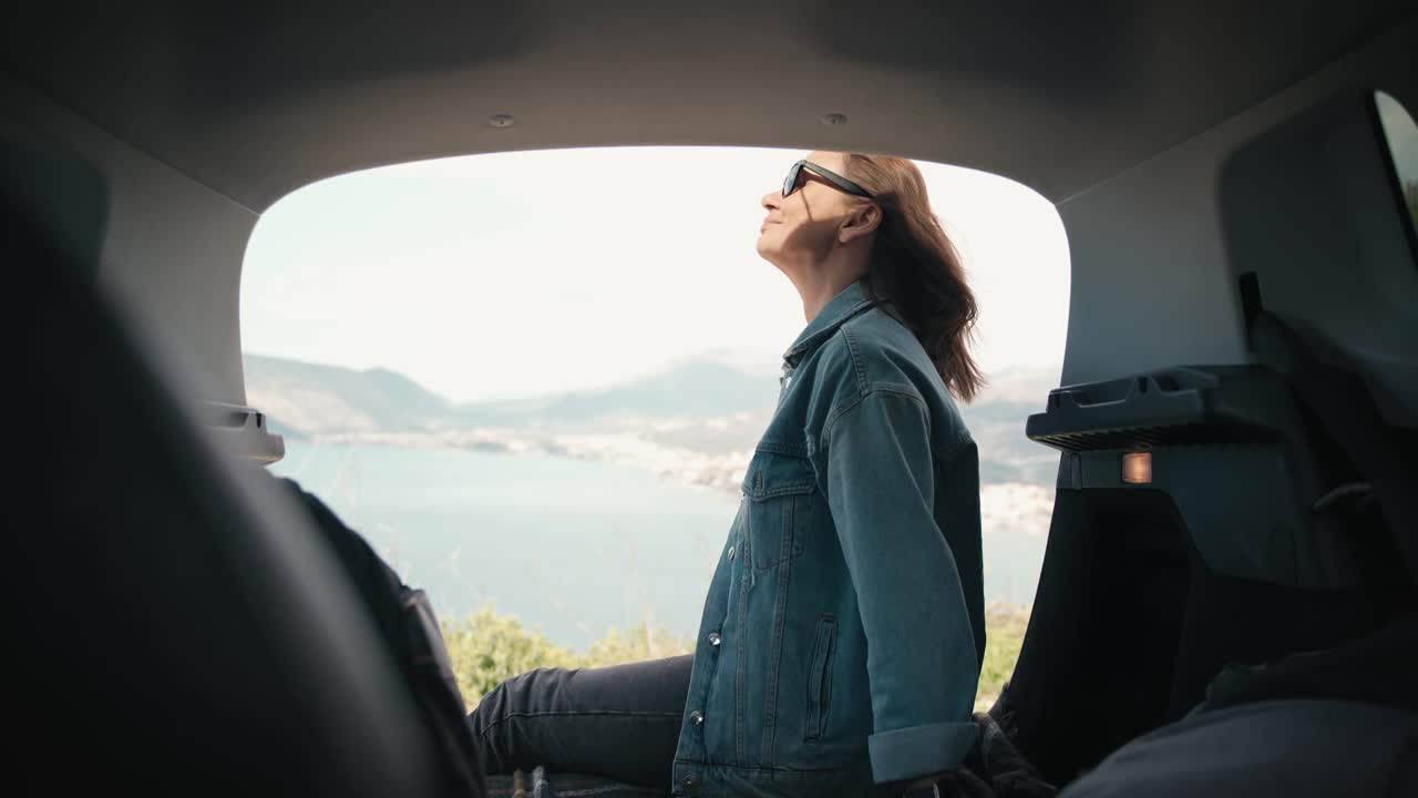 一个女人坐在车的后备箱里欣赏美丽的海景视频下载