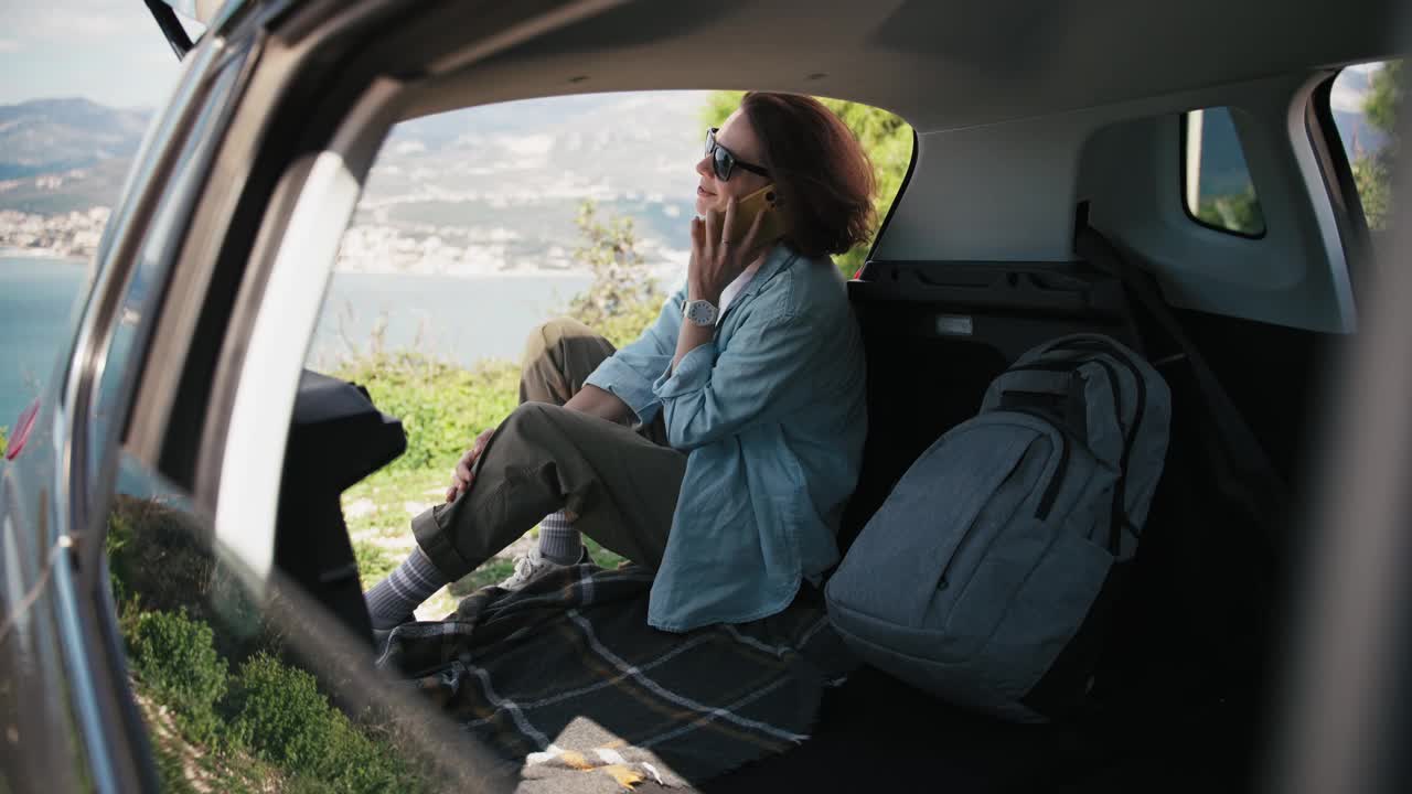 一名年轻女子坐在SUV的后备箱里打电话视频下载