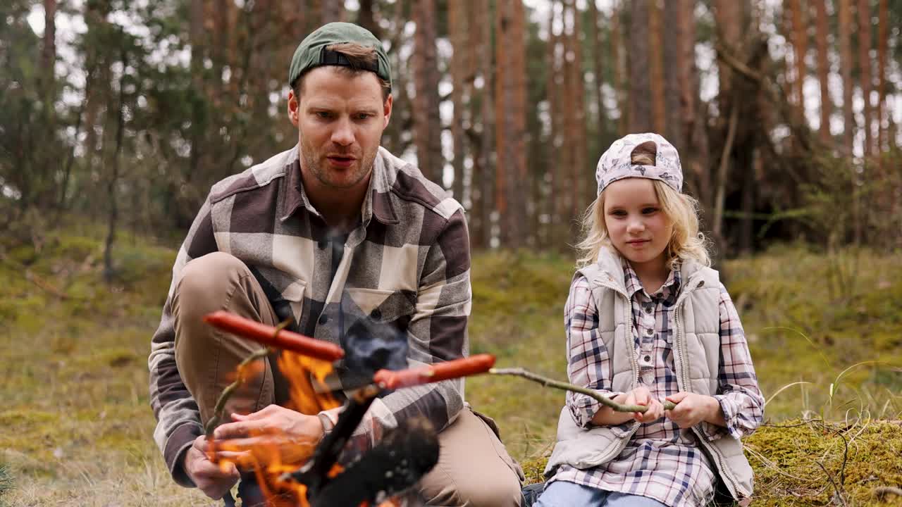 父亲和女儿在森林里的篝火上煎香肠。家庭时光，亲密活动视频下载
