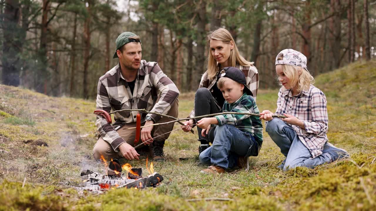一家人带着孩子在森林里露营，在篝火上用木串烤香肠。自然探险，亲密活动视频下载