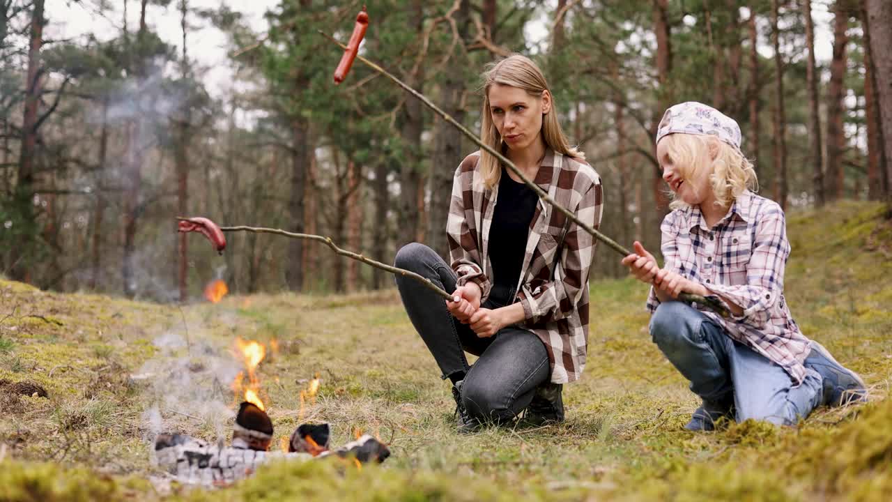 母亲和女儿在森林里的篝火上煎香肠。家庭时光，亲密活动视频下载