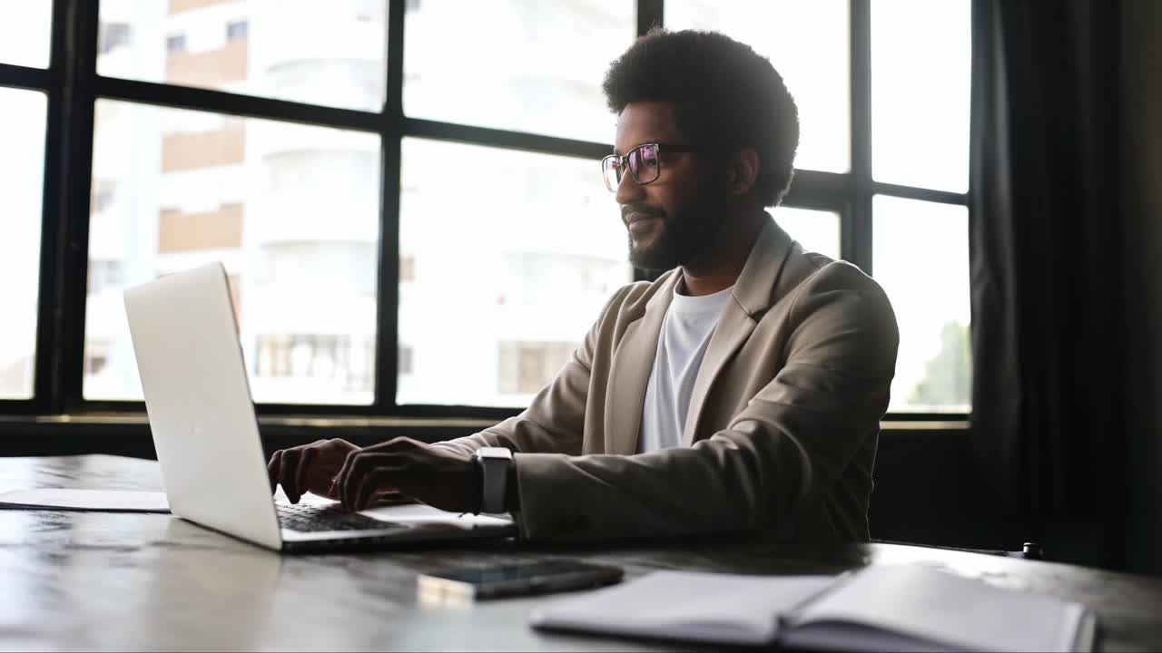 一个留着非洲式发型的开朗的年轻商人正在用笔记本电脑工作视频下载