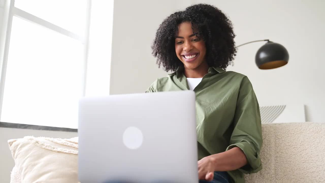 在一个快乐的在线互动时刻，一位非洲裔美国妇女在笔记本电脑上微笑着工作视频下载
