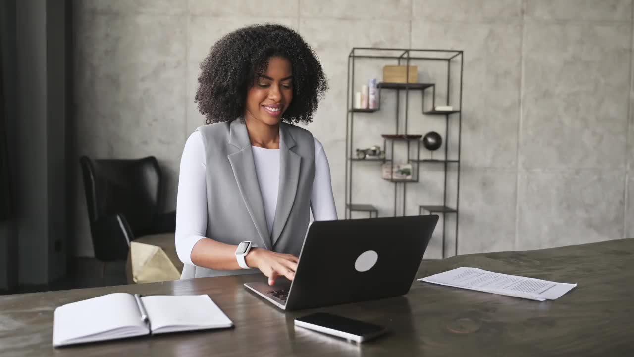 一位面带微笑的非裔美国妇女喜欢在明亮的办公室里用笔记本电脑工作视频下载