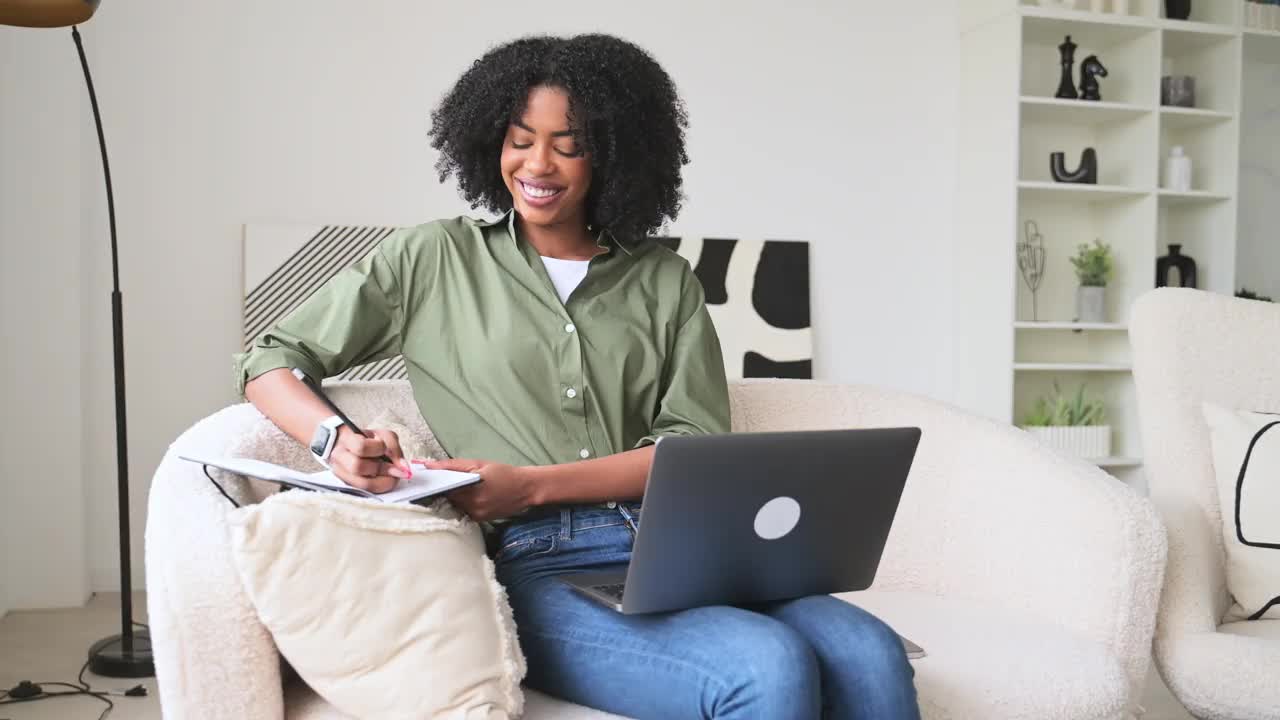 一位满足的非裔美国女性从事多任务处理，在笔记本上写作视频下载