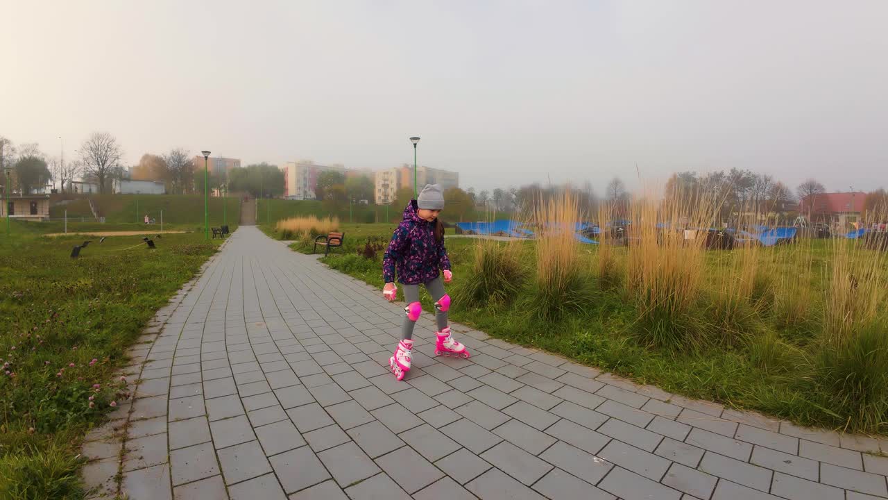 戴着护膝和护肘的小女孩在城市公园户外学习溜冰。孩子们喜欢积极的运动，广角视野视频下载