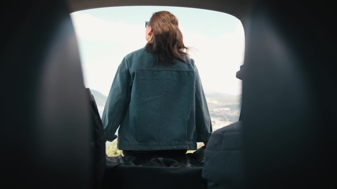 一个女人坐在车的后备箱里欣赏美丽的海景视频下载