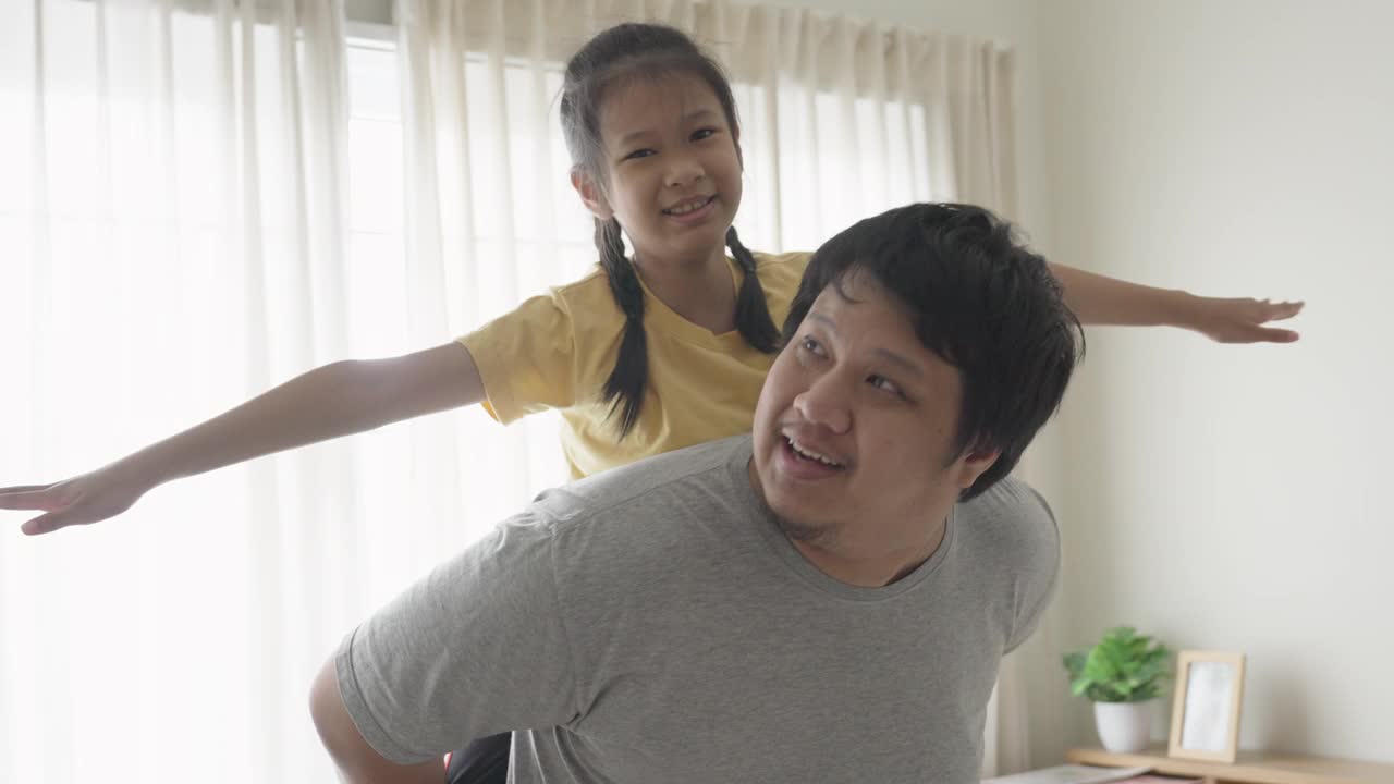 开朗的亚洲女孩喜欢和她的父亲一起玩，微笑着骑在背上视频下载