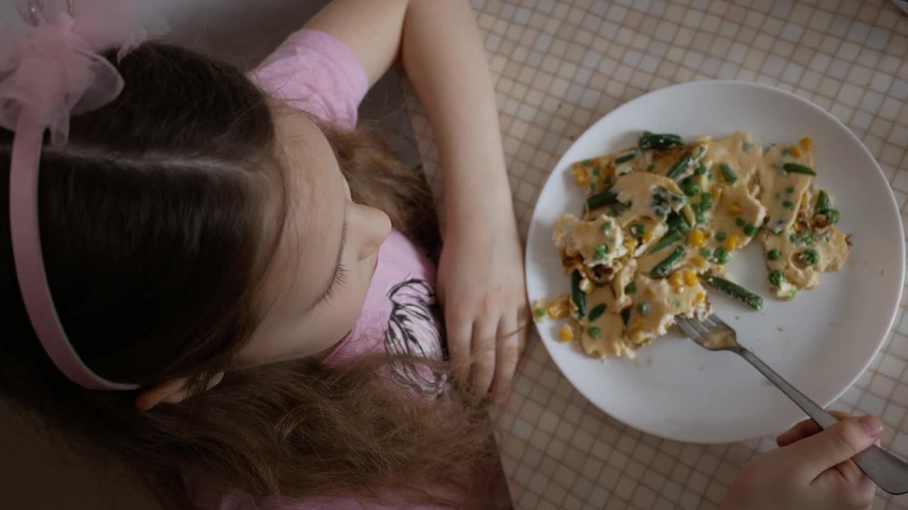 小女孩早餐吃蔬菜煎蛋卷。孩子饿了，胃口很大。家庭食物和烹饪的概念。从上面看视频下载