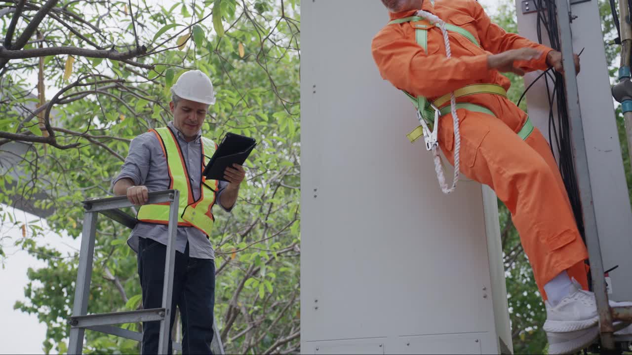 两名身穿防护服的男工程师在野外检查通讯塔的功能，讨论维修方案。视频下载