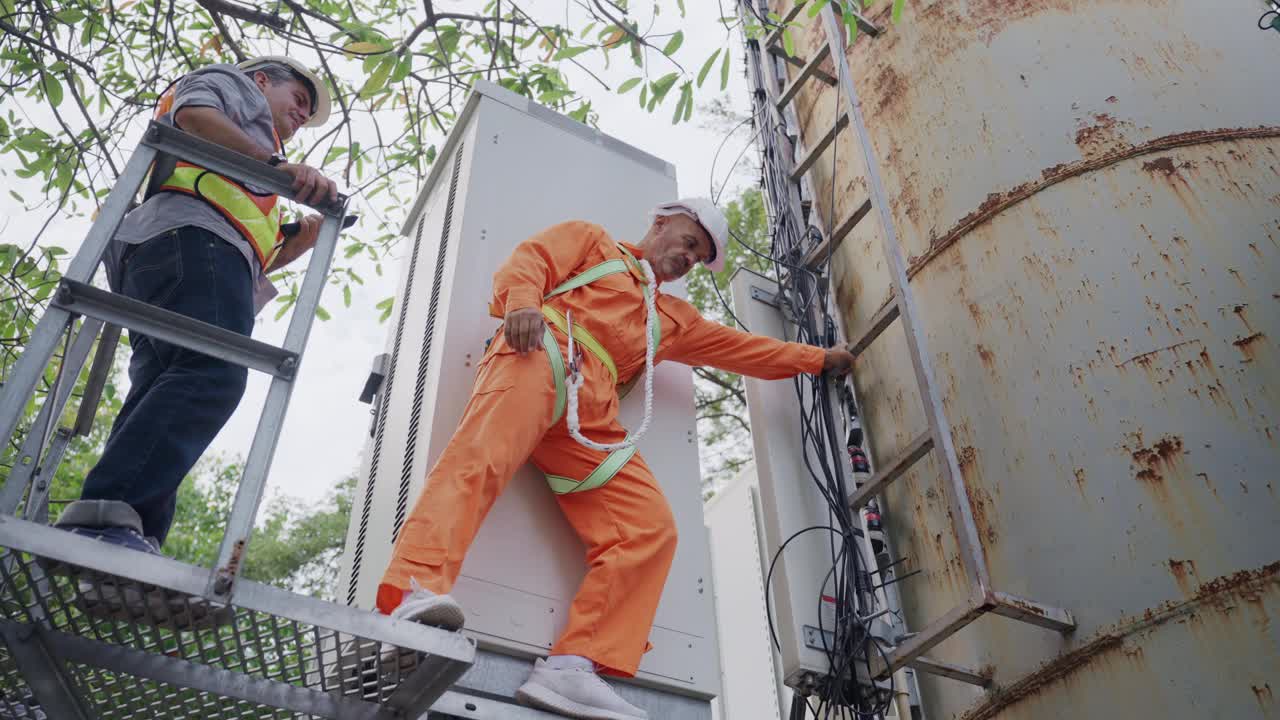 高级技术人员穿着橙色工作服，头戴防护帽，爬上通讯水梯，同事用数码平板电脑检查问题，指导技术人员维修。视频下载