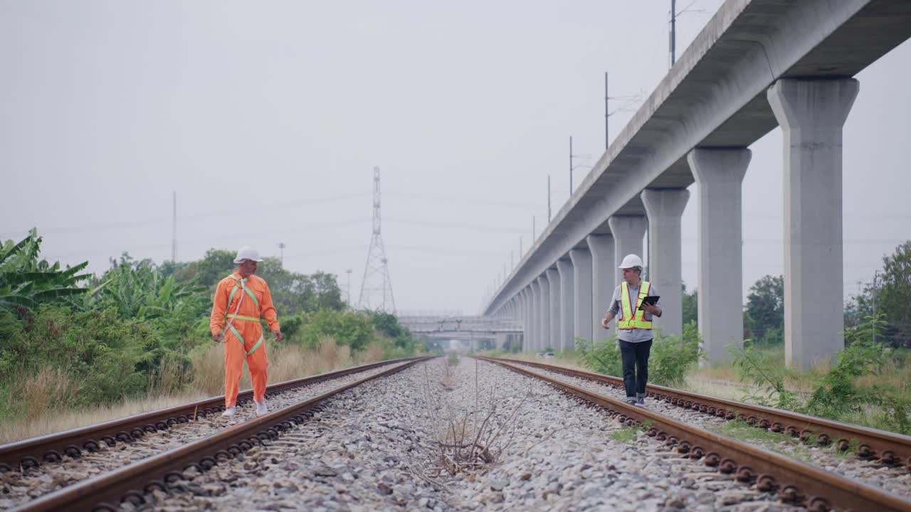 两名男性工程师与防护工作服一起工作，走在铁轨上，同时调查轨道维护计划。视频下载