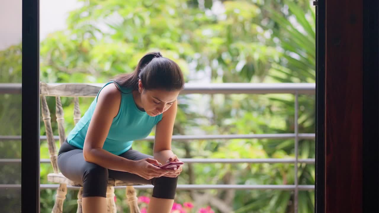西班牙年轻女子在锻炼后坐在阳台的椅子上上网视频下载