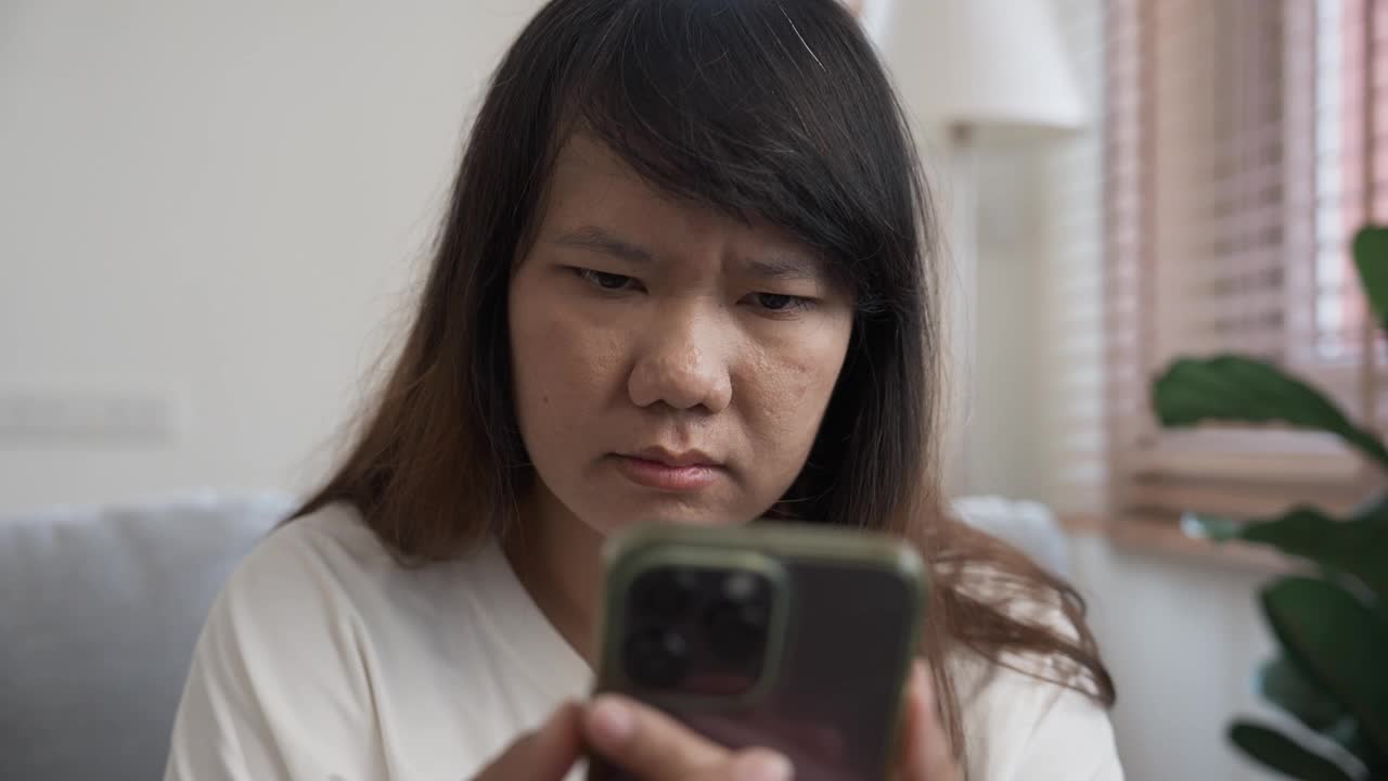 担心的女人在家里使用智能手机视频下载