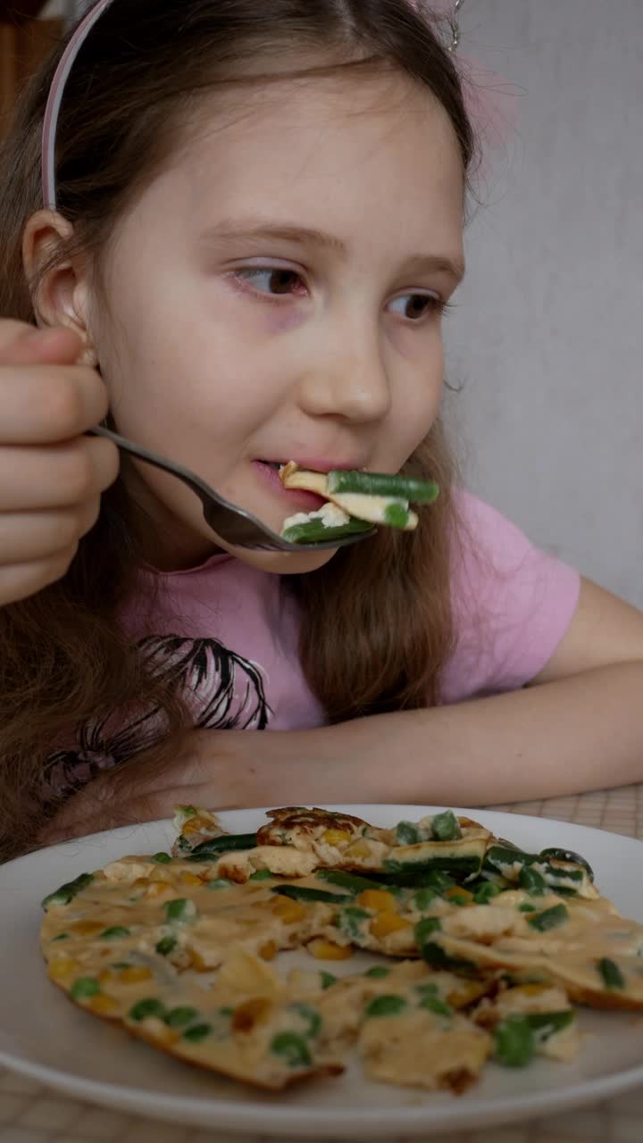 垂直格式。小女孩早餐吃煎蛋卷配蔬菜。孩子饿了，胃口很大。家庭食物和烹饪的概念。视频下载