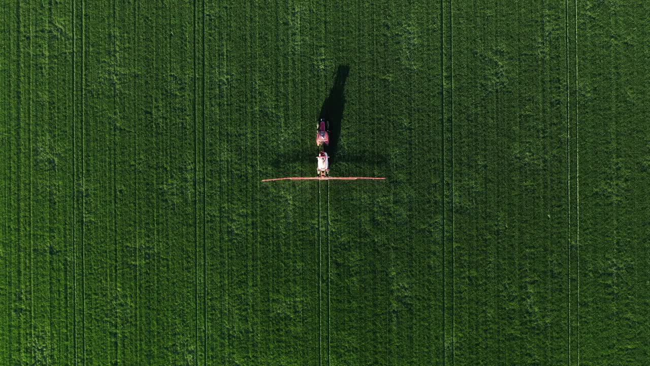 无人机拍摄的农用拖拉机与作物喷雾器在小麦种植区喷洒除草剂的航拍照片视频下载