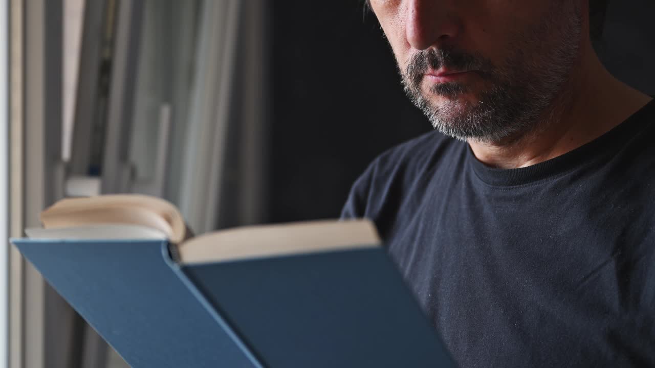 一个成年男子在客厅窗边看书的特写镜头视频下载