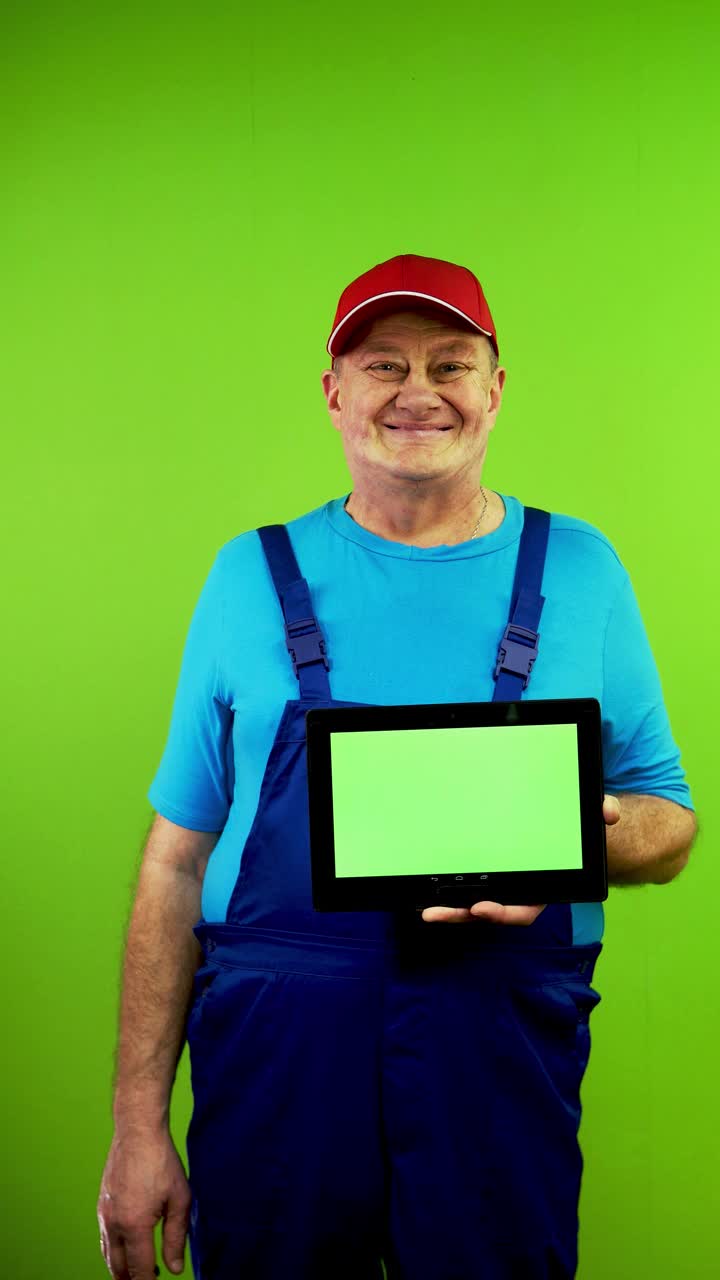 穿着工作服的高级修理工正在展示带有空白广告显示屏的平板电脑。视频下载