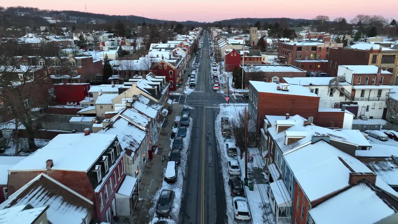 美国小镇上积雪的主要街道上的空中直线飞行。汽车行驶在把小商店和房子隔开的街道上。美丽的冬日黄昏。视频下载