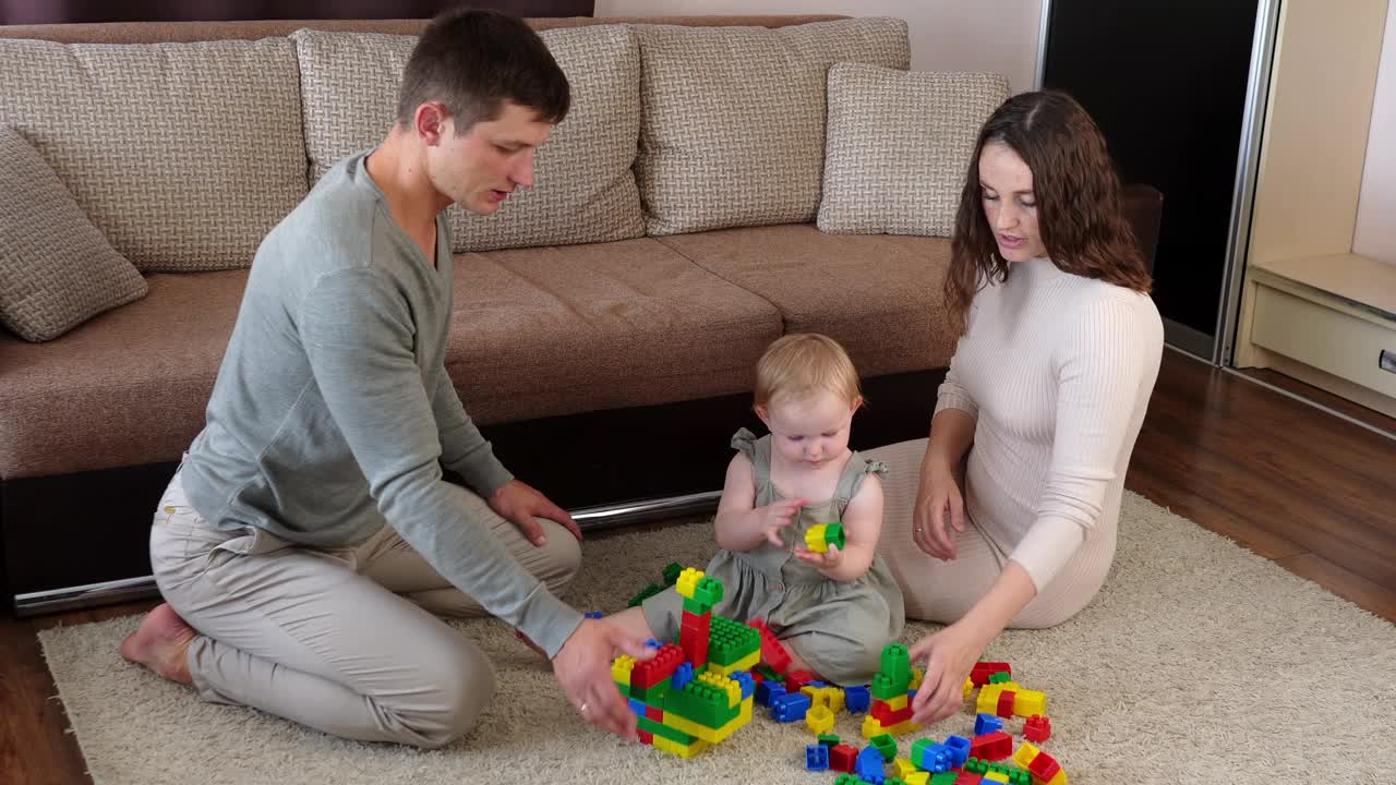 年轻的家庭带着孩子在家里的地毯上玩冰壶游戏，搭积木。妈妈、爸爸和孩子一起度过闲暇时光，为孩子在教育活动中取得成功而欢呼，掌声视频下载