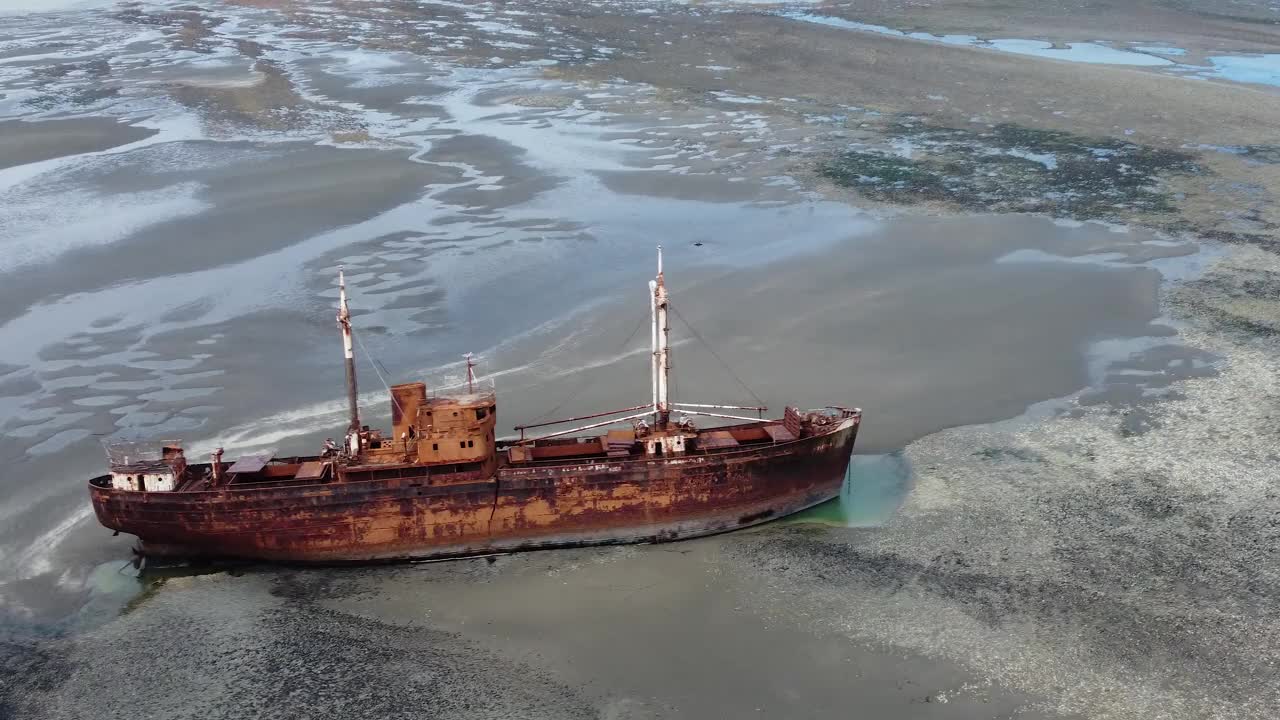退潮时，相机环绕着一艘躺在沙滩上的生锈的旧船残骸，背景是大海视频下载