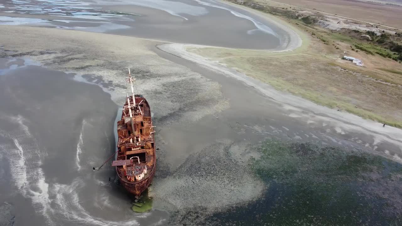 退潮时，相机环绕着一艘躺在沙滩上的生锈的旧船残骸，背景是陆地视频下载