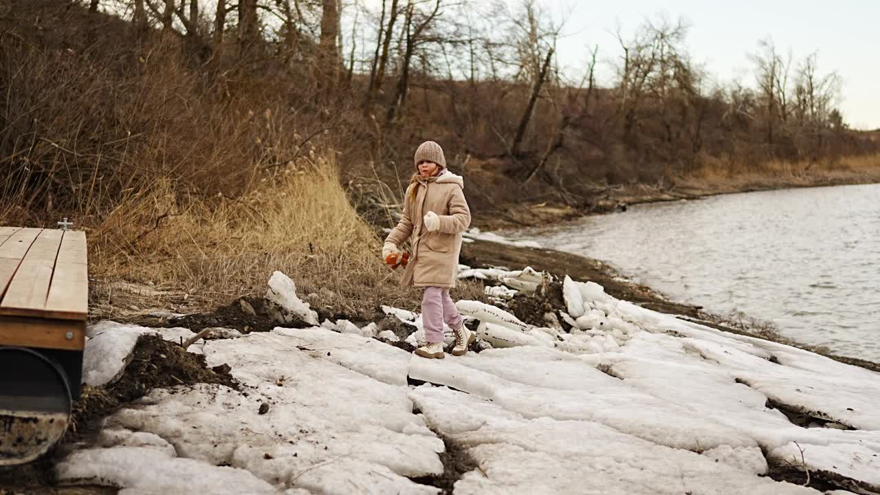 十几岁的女孩穿着冬装走在河岸的冰上。视频下载