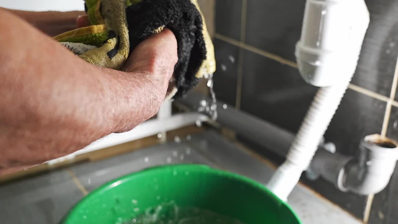 由于浴室漏水，一名男子用抹布在桶里收集水。视频下载