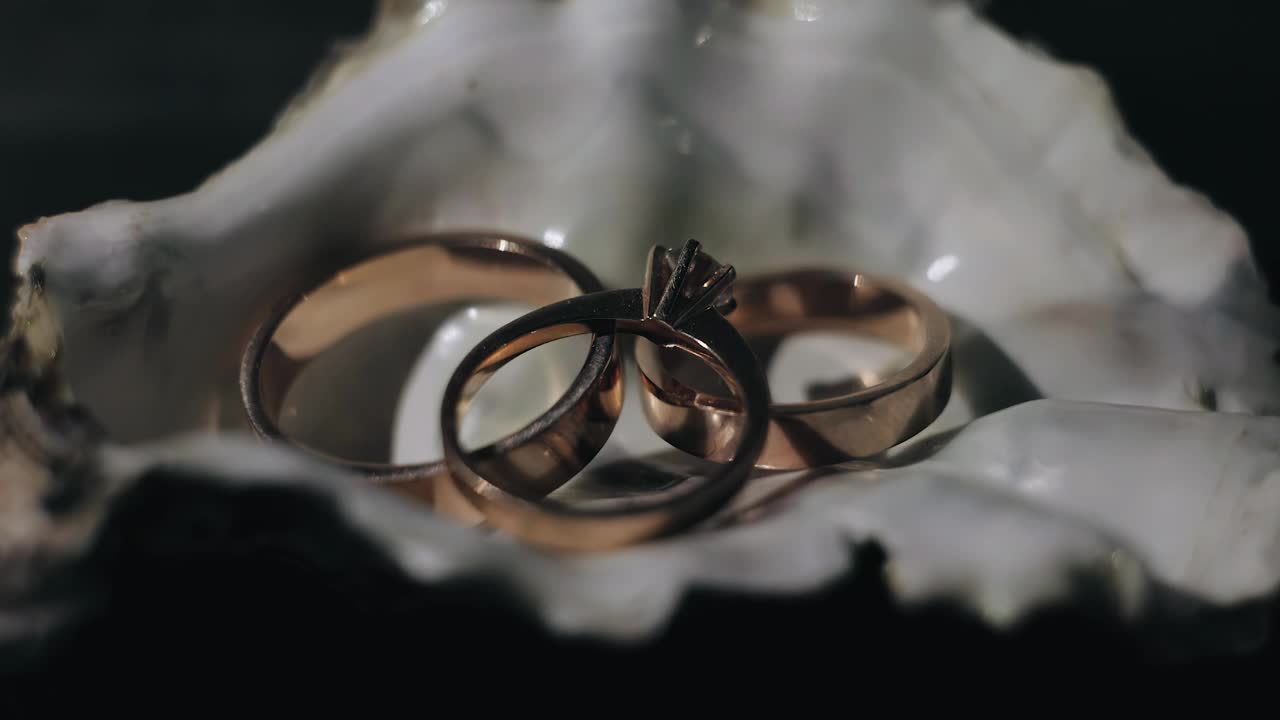 金戒指放在桌子和鲜花上，被动态光照亮。近距离拍摄视频下载